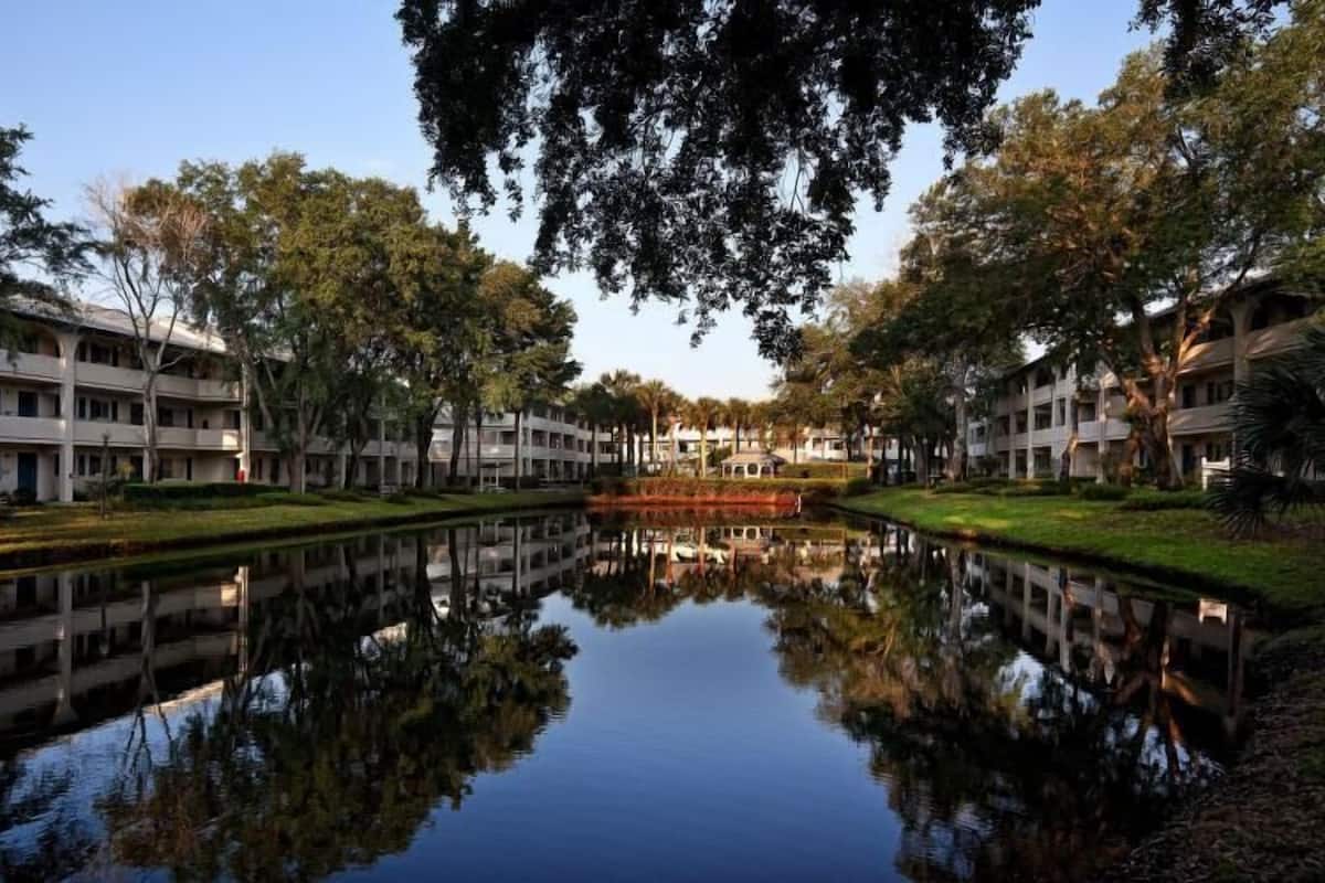 A building with multiple floors, a central courtyard with a reflective water feature, and surrounding trees.