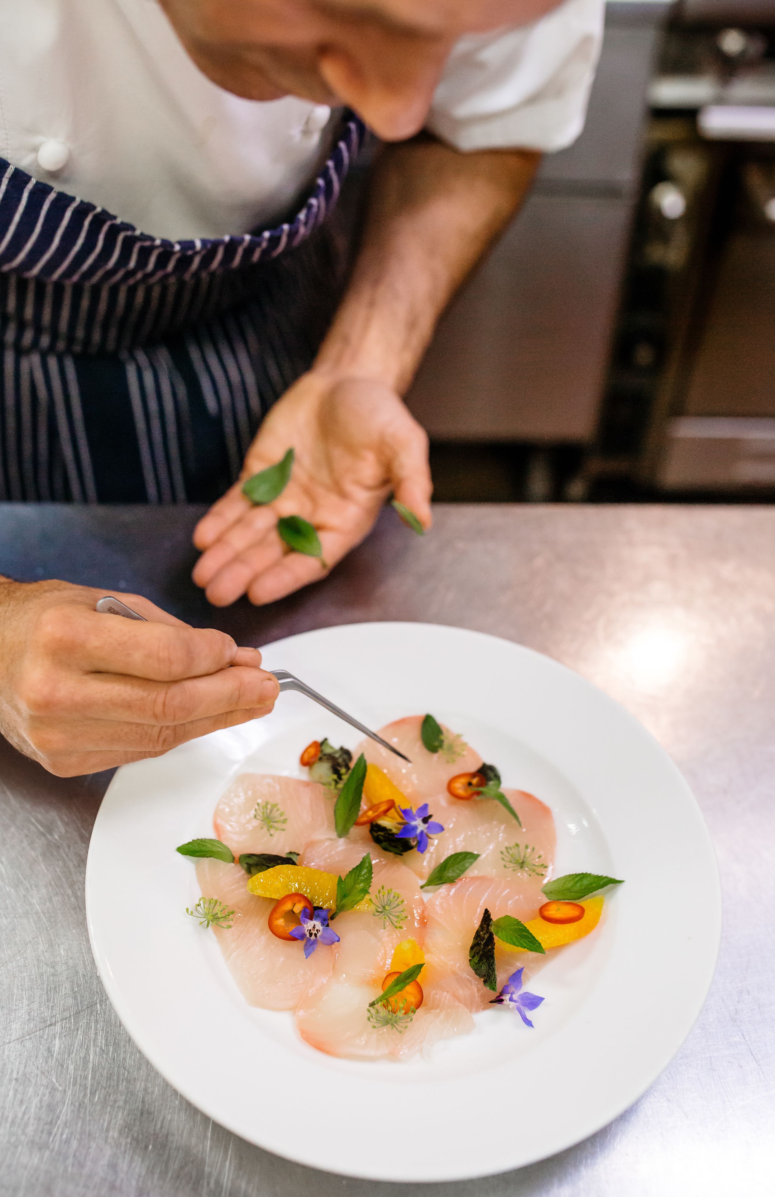 A chef preparing a dish with a white plate, garnished with herbs and flowers.