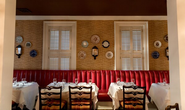 Un restaurante con zona de asientos en una cabina roja, mesas blancas y platos decorativos en la pared.