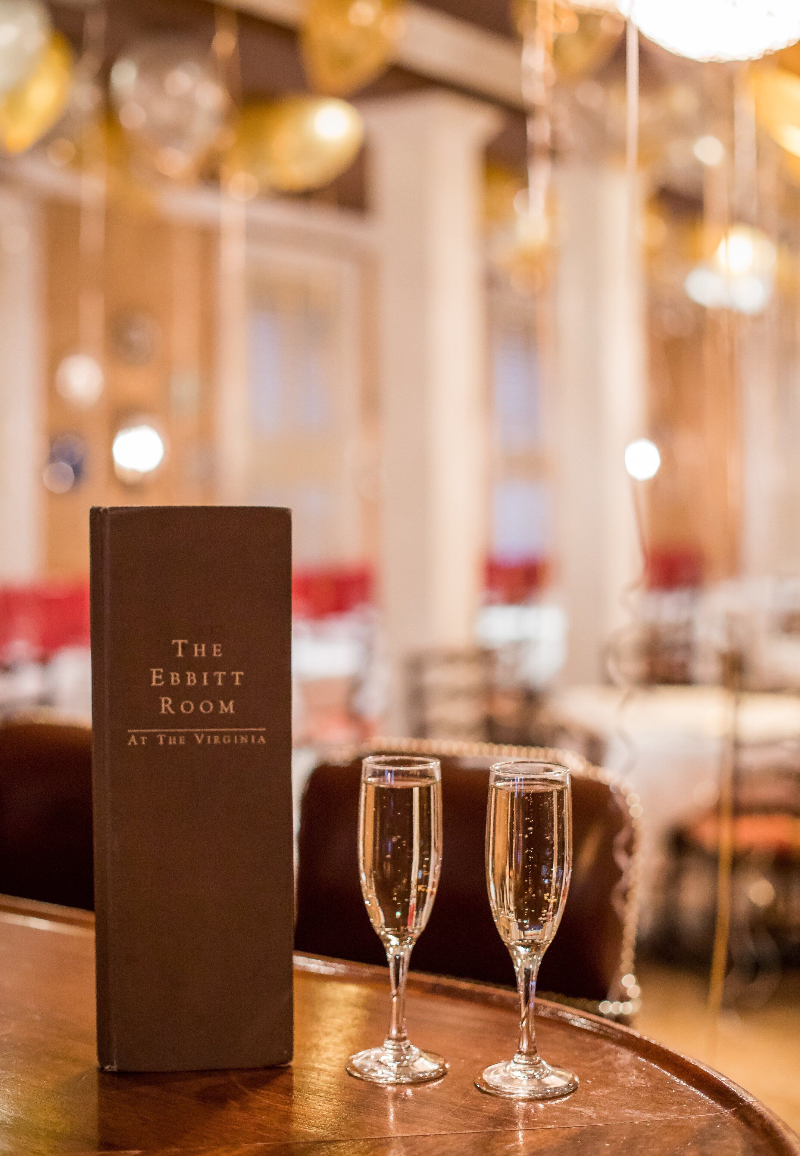 Un menú con el título "The Ebbitt Room" en The Virginia, con dos copas de champán sobre una bandeja de madera.