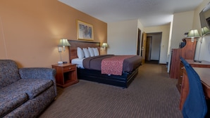 A hotel room with a bed, a desk, a chair, a couch, and a lamp. - Thunderbird Lodge (Mitchell)