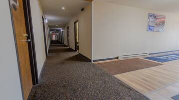 A hotel hallway with carpeted floors, a wooden door labeled "44", and a poster on the wall.