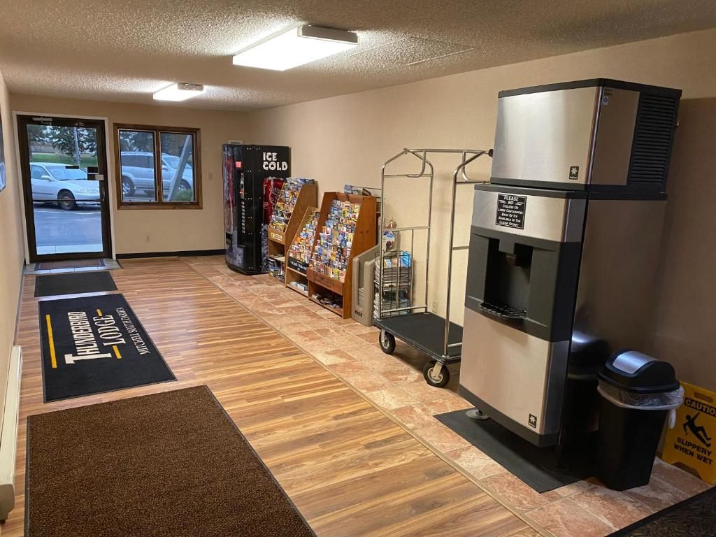 A hotel lobby with a reception desk, a coffee machine, a trash bin, and a window with a view of parked cars outside.