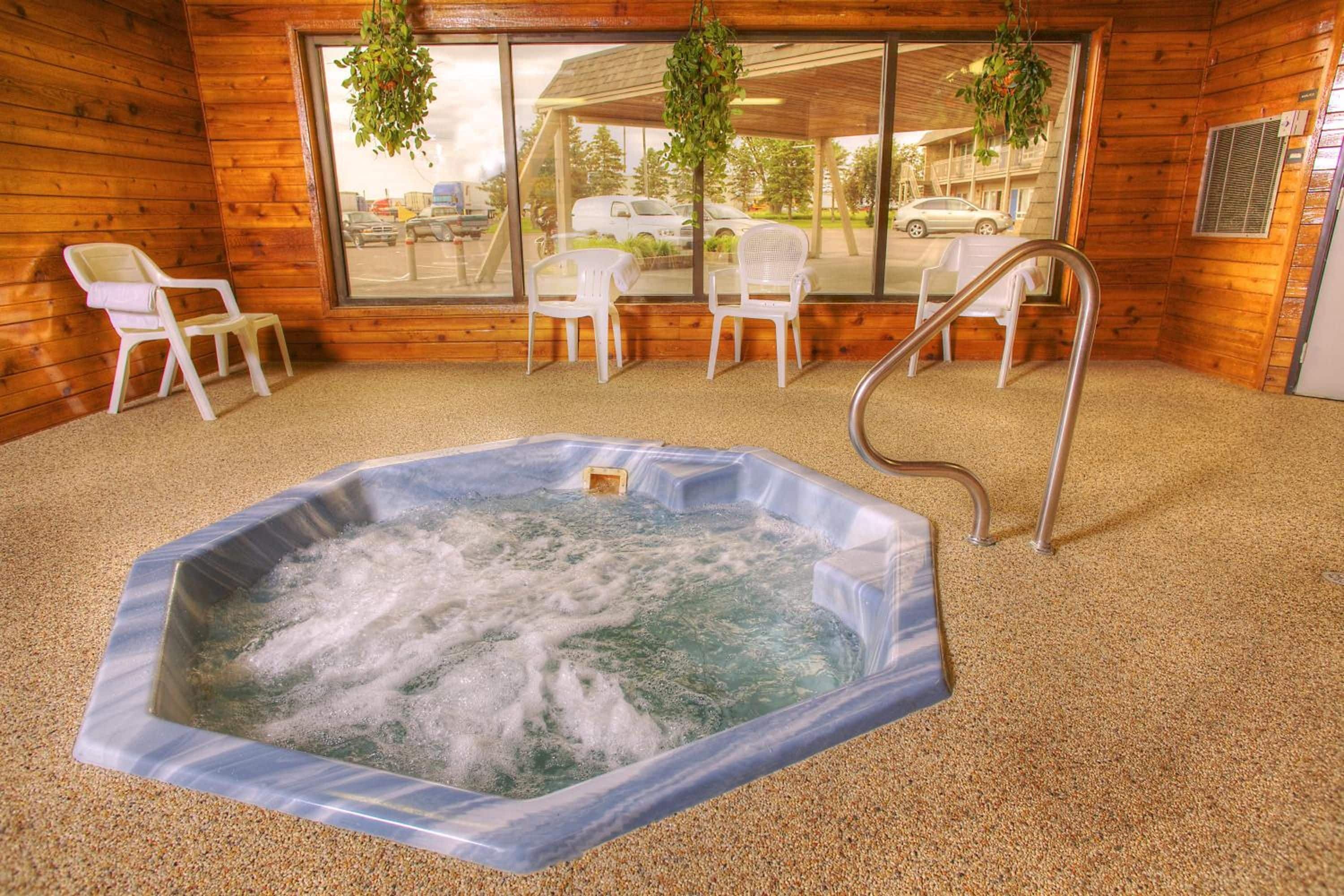Ein Whirlpool in einer Holzhütte mit Blick auf parkende Autos vor der Tür.