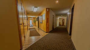 A hotel hallway with wooden paneling, a patterned carpet, and a clock on the wall. - Thunderbird Lodge (Mitchell)