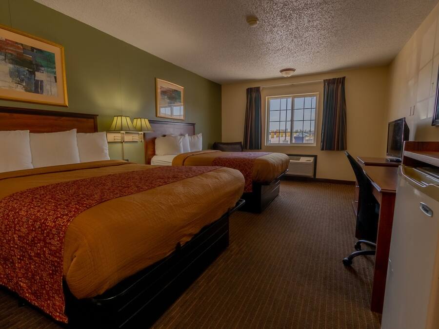 A hotel room with two beds, a desk, a television, and a window with curtains.