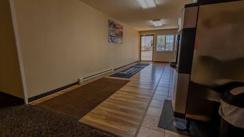 A hallway with a wooden floor, a brown doormat, a poster on the wall, and a door leading outside.