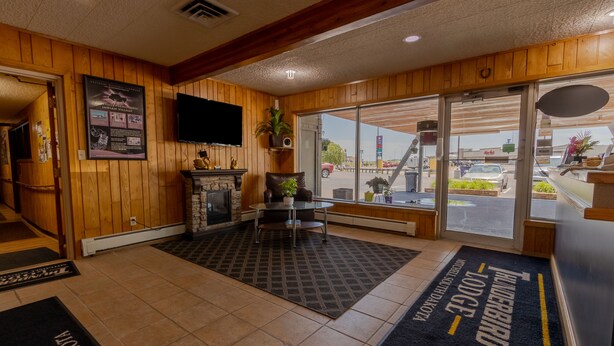 A hotel lobby with wooden walls, a fireplace, a television, and a view of the parking lot. - Thunderbird Lodge (Mitchell)