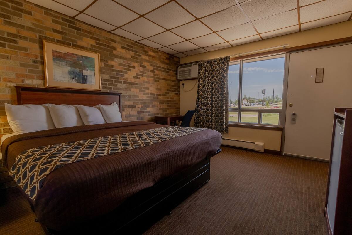 Ein Hotelzimmer mit einem großen Bett, einer Wand mit Ziegeloptik, einem Fenster mit Aussicht und einer Klimaanlage.
