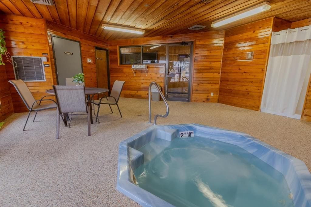 A wooden cabin interior with a hot tub, seating area, and a door leading outside.