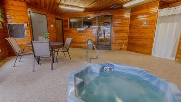 A wooden cabin interior with a hot tub, seating area, and a door leading outside.