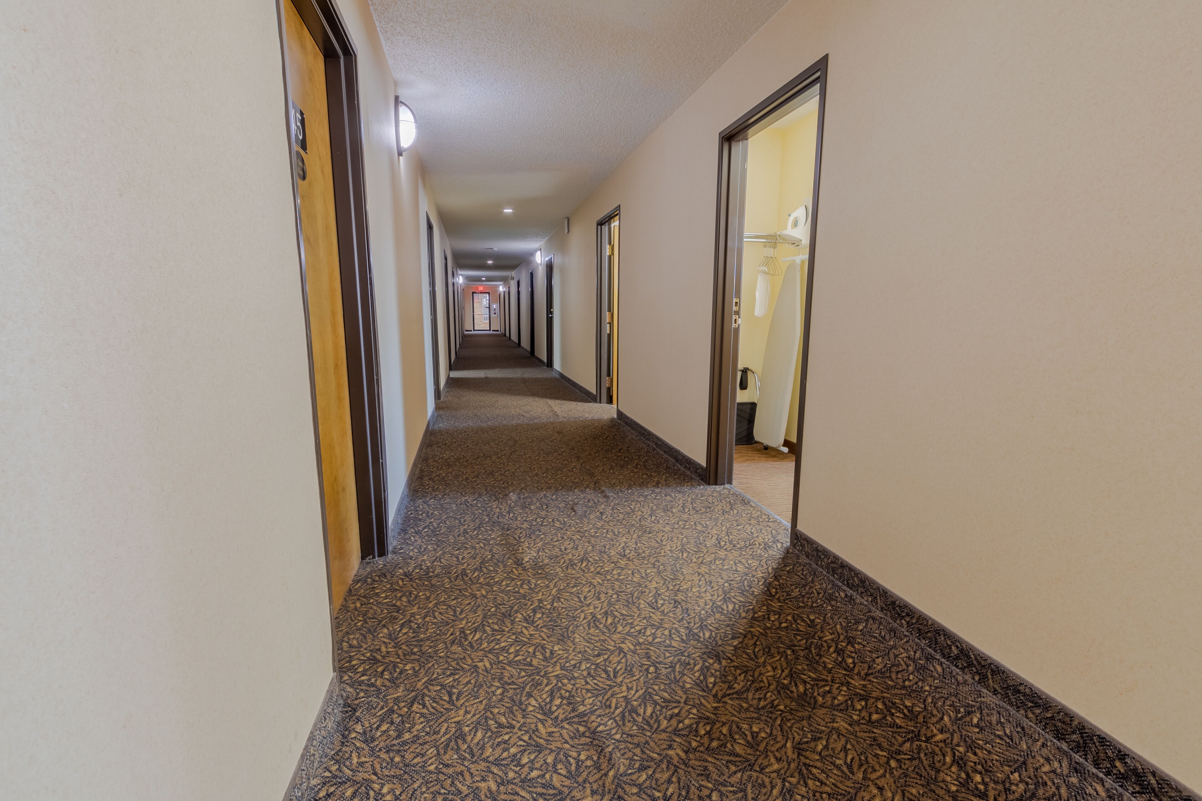 Un largo y estrecho pasillo de hotel con alfombra estampada, puertas a ambos lados y una lámpara en el techo.