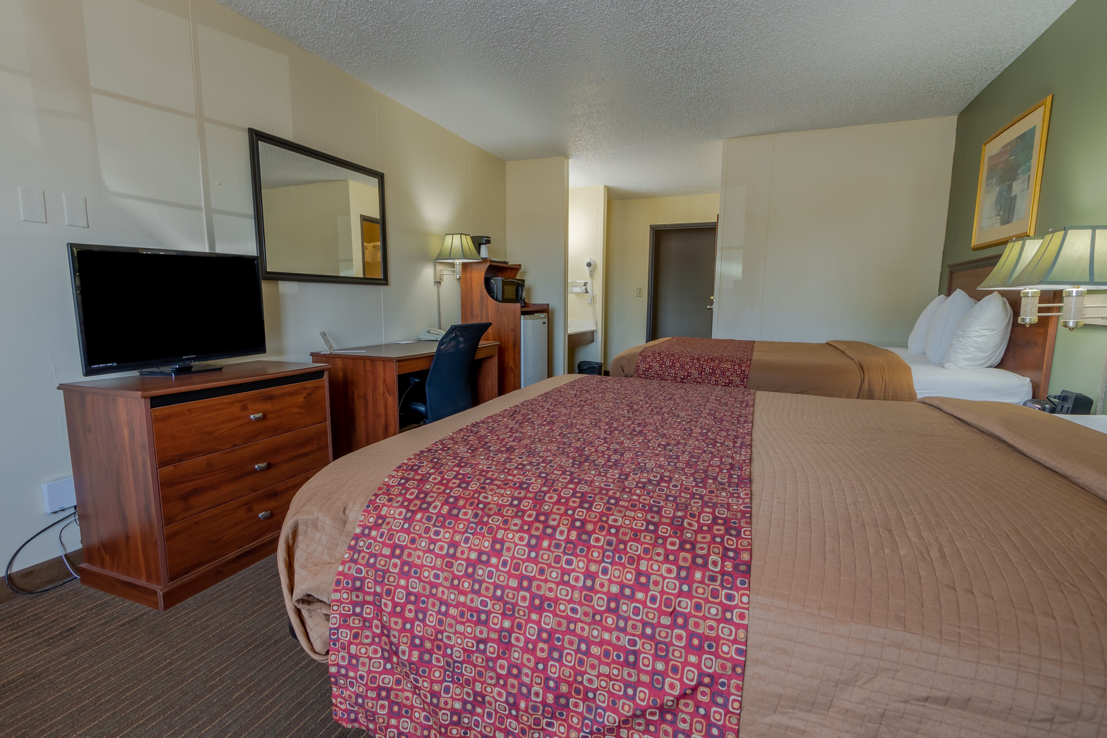 A hotel room with a bed, a desk with a computer, a TV, and a dresser.