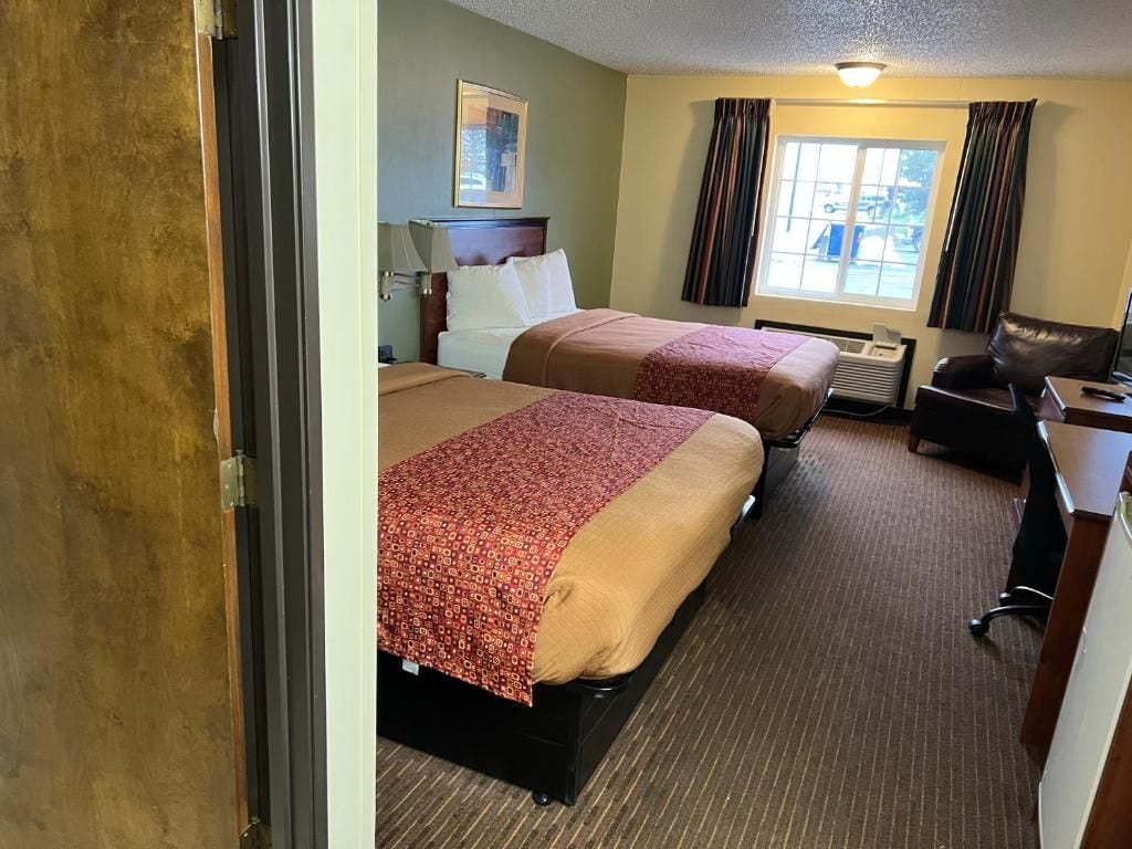 Habitación de hotel con dos camas, un escritorio, una silla y una ventana con cortinas.