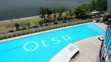 A swimming pool with the name 'Otsu' on the water, surrounded by a paved deck and a view of a road and greenery.
