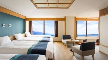 Habitación de hotel con tres camas, zona de estar con una mesa y ventanas amplias que ofrecen vistas.