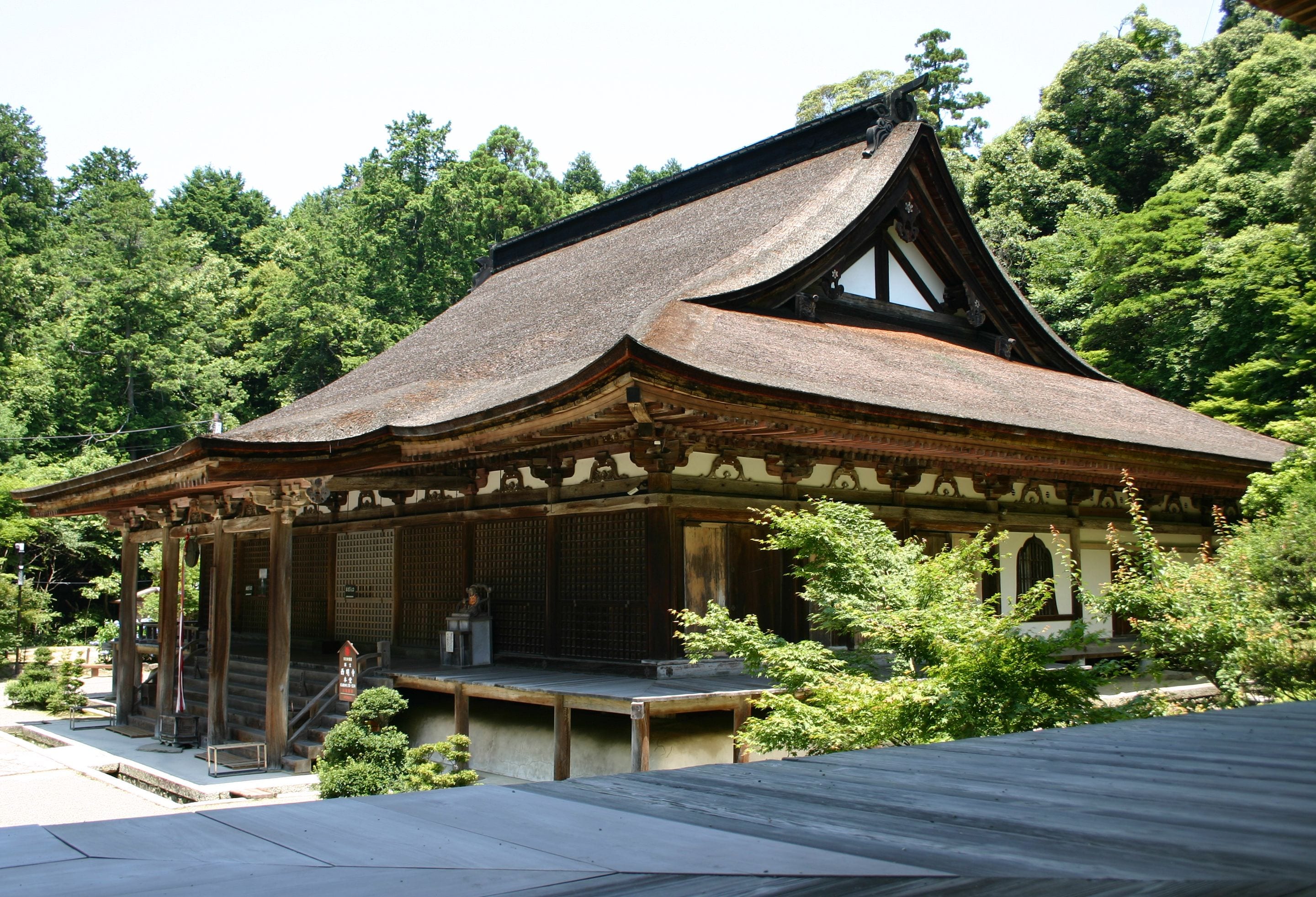 A traditional wooden building with a sloped roof, surrounded by lush greenery.