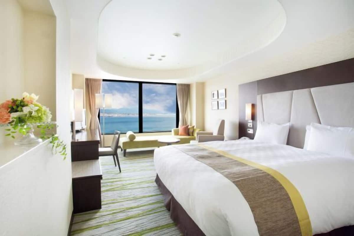 A hotel room with a large bed, a desk, a chair, a sofa, and a view of the ocean.