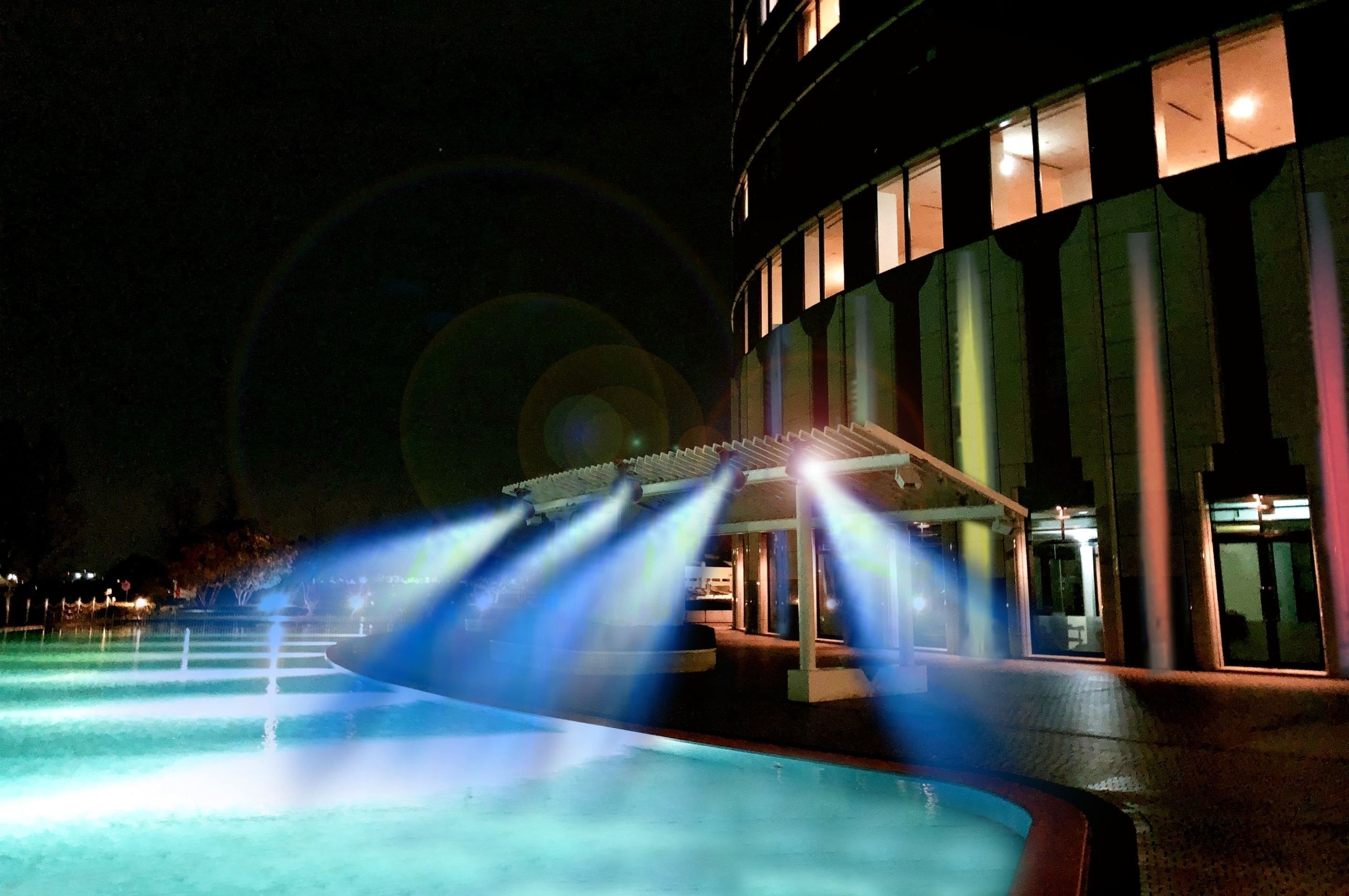 A nighttime pool area with water features and a building with illuminated windows.