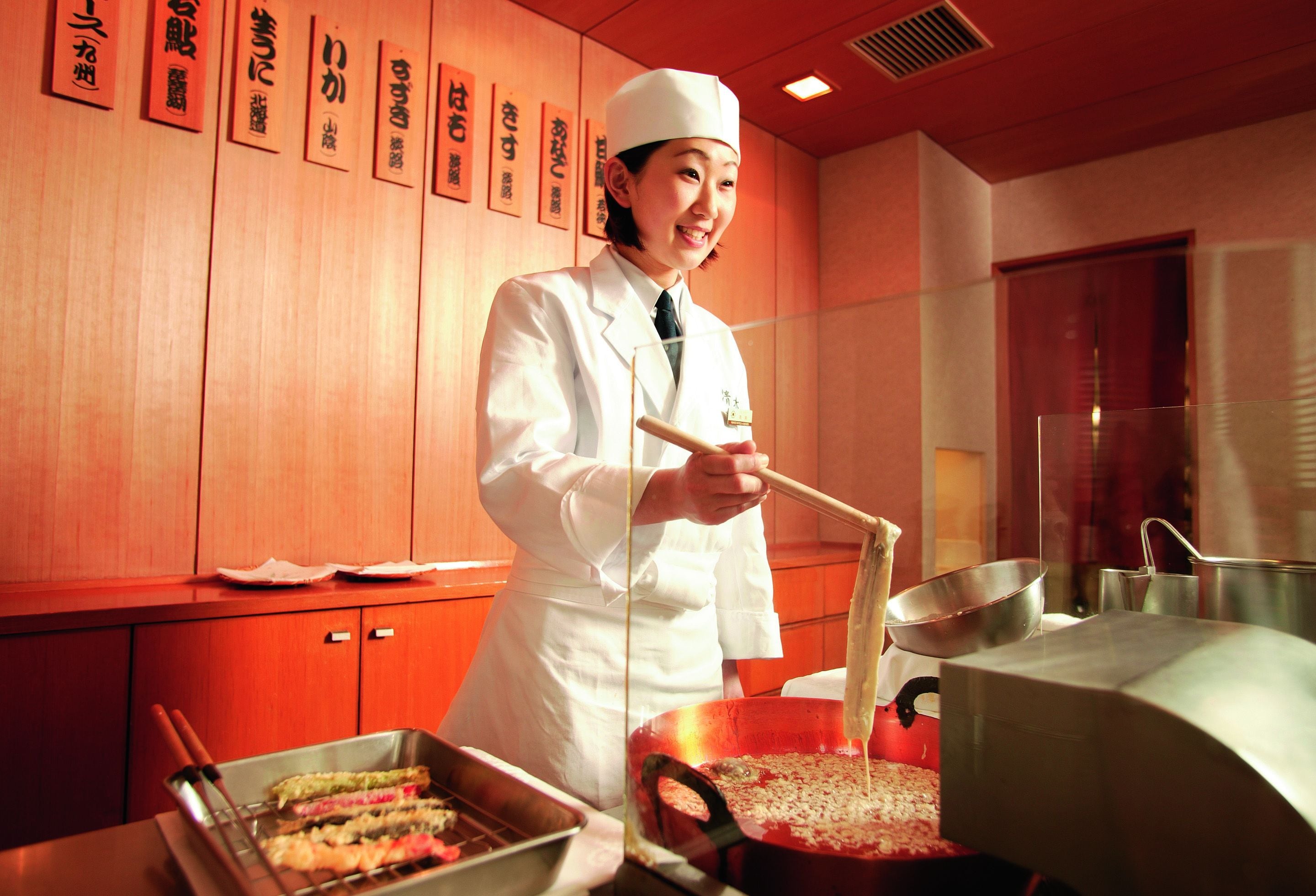 A chef in a white uniform cooking in a kitchen with wooden walls and a red ceiling.