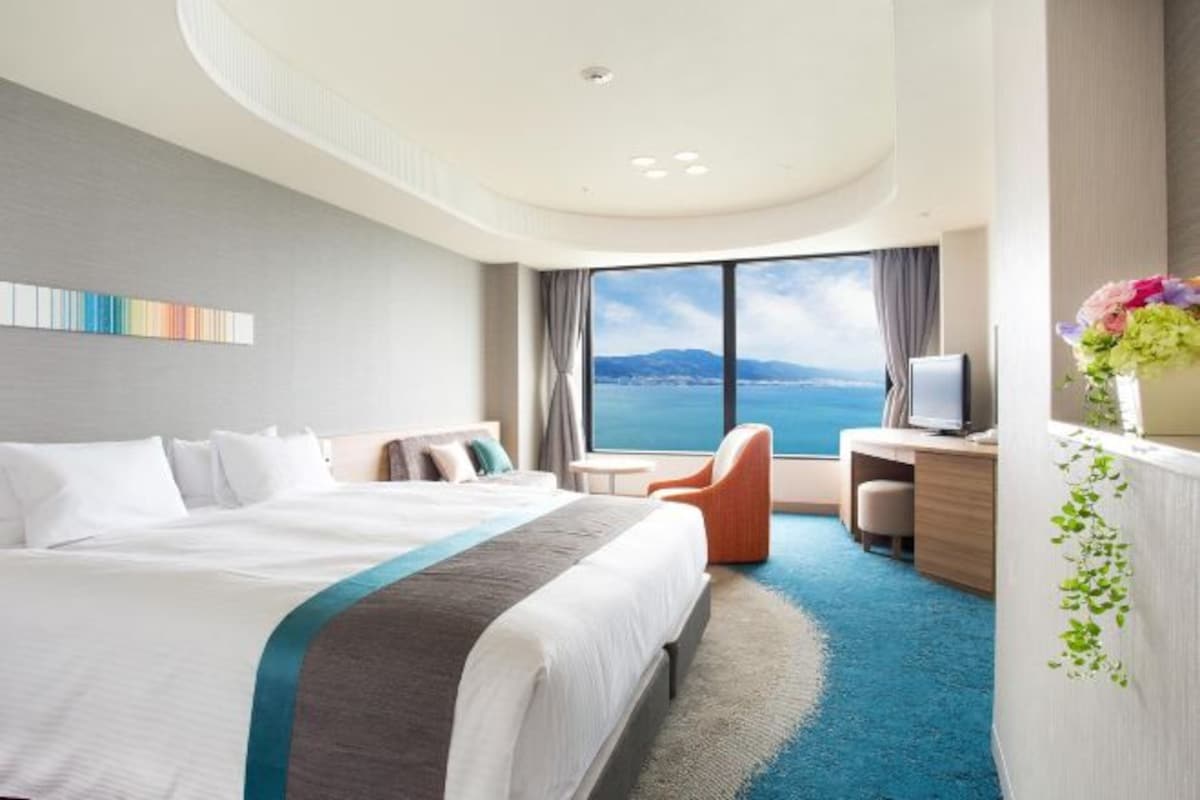 A hotel room with a large bed, a desk, a chair, and a view of the sea.