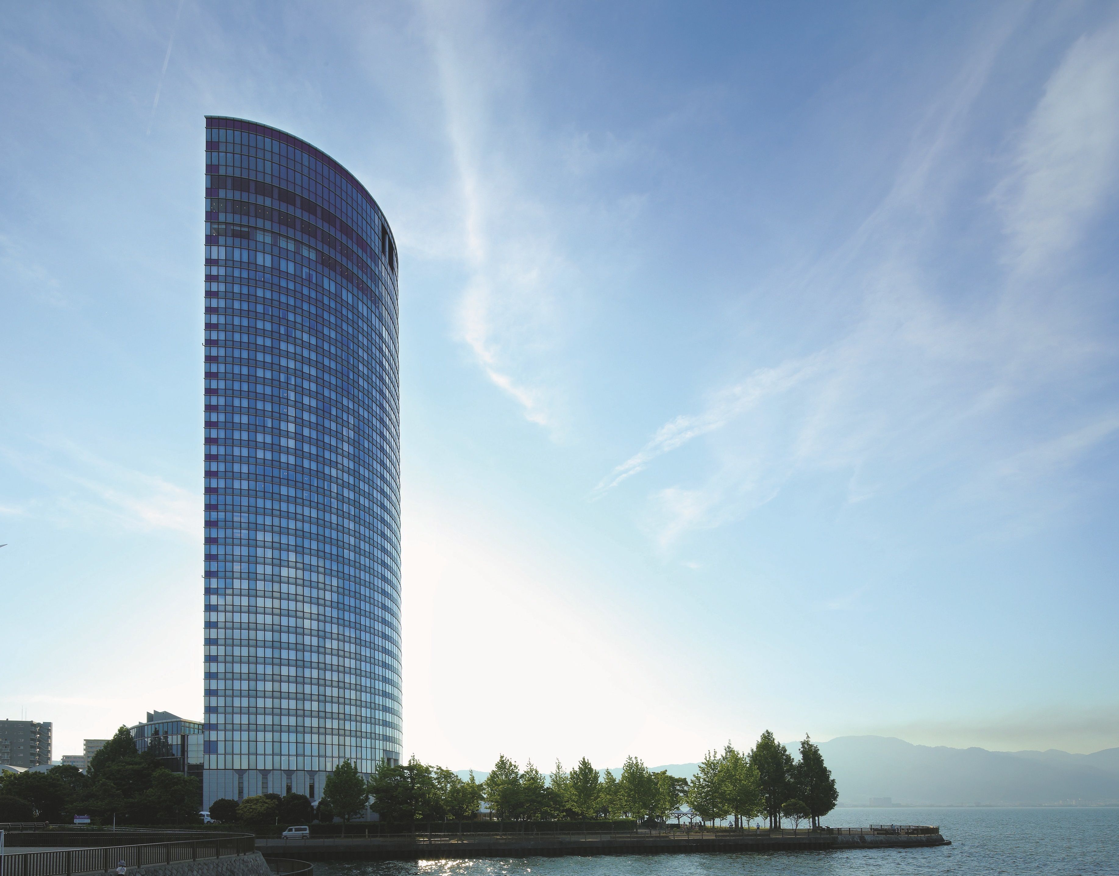 A tall, curved glass building with a clear sky and distant mountains.