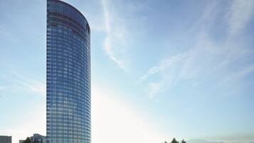A tall, curved glass building with a clear sky and distant mountains.