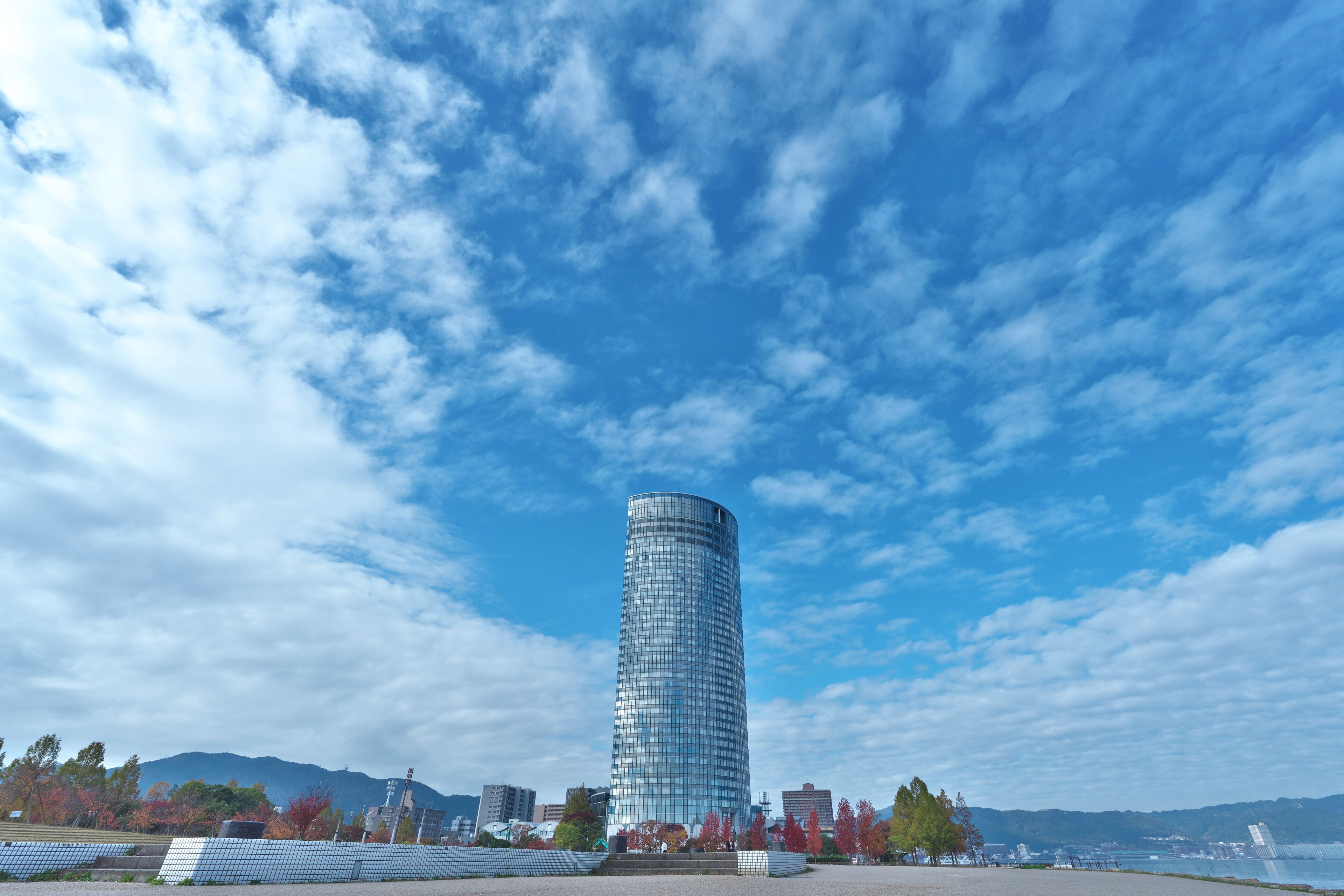 A modern skyscraper with a curved design, surrounded by trees and a clear sky.
