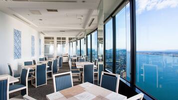 Un comedor moderno con mesas y sillas, con ventanas amplias que ofrecen vistas a la ciudad y al agua.