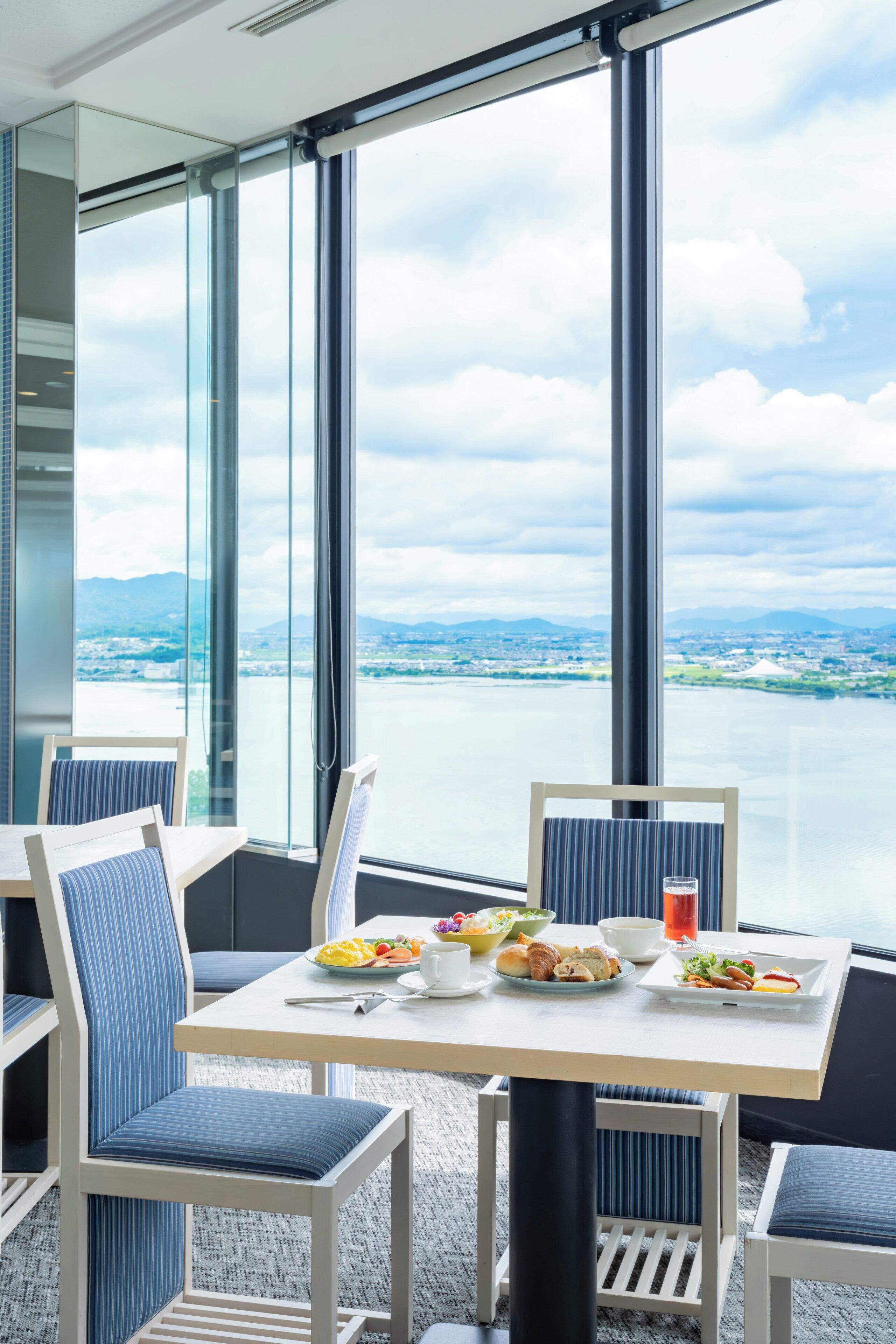 Un coin repas avec une table dressée pour deux personnes, de grandes fenêtres offrant une vue sur une étendue d’eau et un paysage lointain.