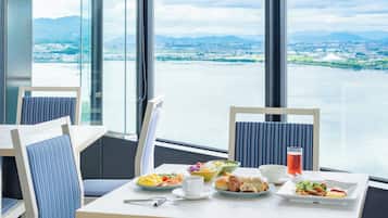 Een eetgedeelte met een tafel voor twee personen, grote ramen met uitzicht op een waterpartij en een verafgelegen landschap.