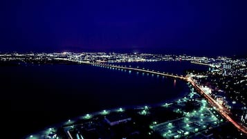 Vista aérea de una ciudad costera de noche, con un puente destacado, calles iluminadas y un puerto deportivo.