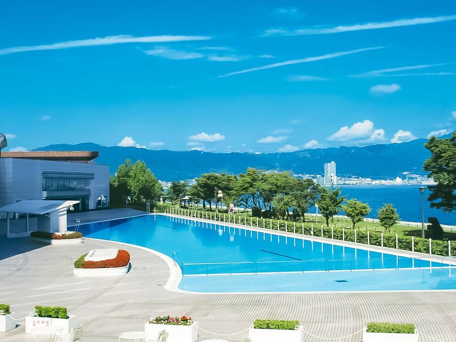 Un hotel moderno con una amplia piscina, vistas al mar y montañas al fondo.