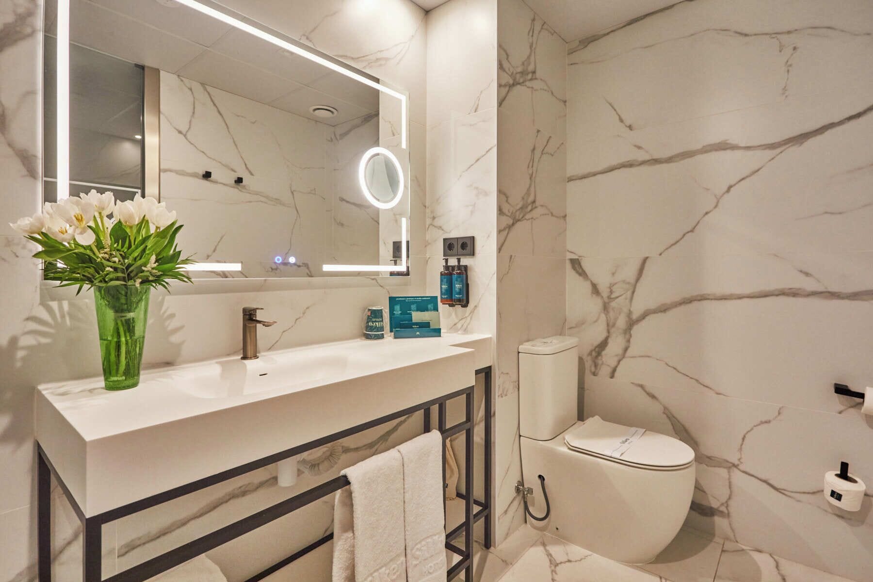 Un baño moderno con salpicadero de mármol, tocador con espejo, inodoro y zona de ducha.