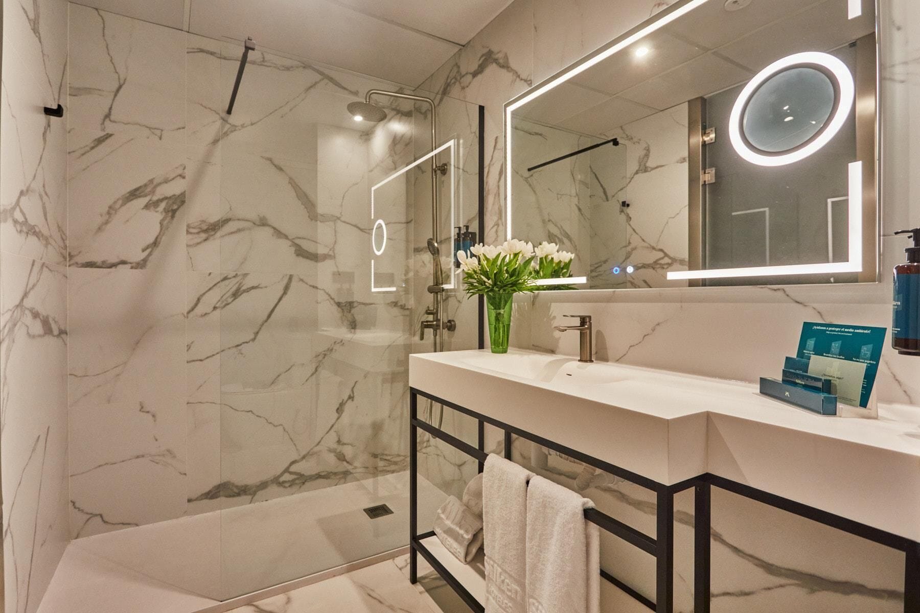 A modern bathroom with a marble wall, a glass shower enclosure, a vanity with a mirror, and a towel rack.