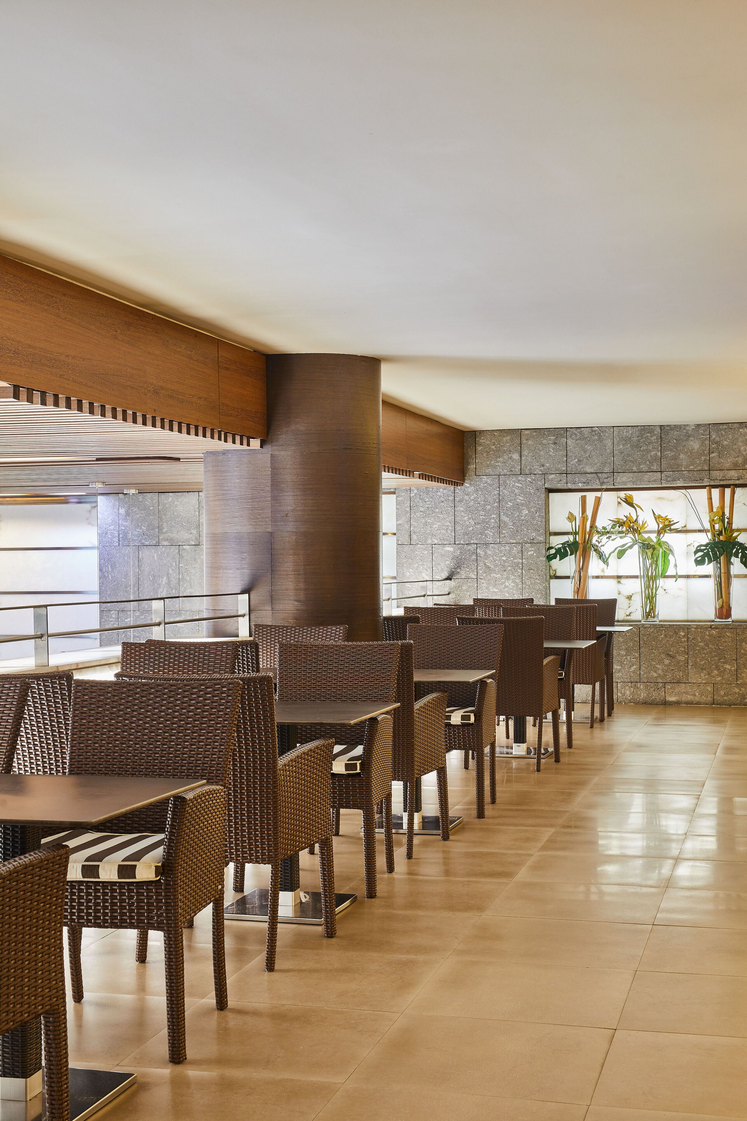 Un restaurante con mobiliario de mimbre, pared de piedra y ventana con plantas.
