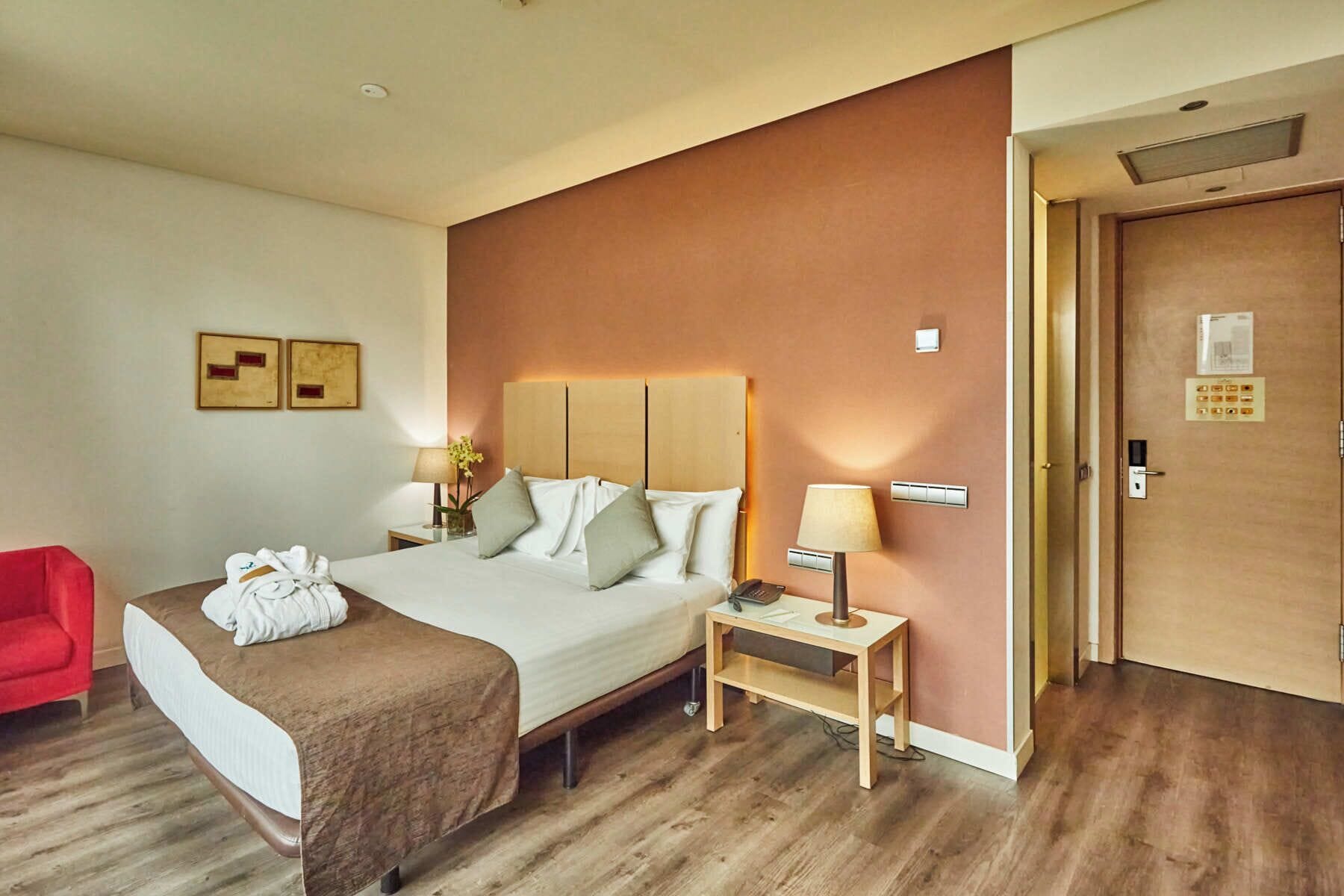 Una habitación de hotel con cama, mesita de noche, lámpara y una silla roja.