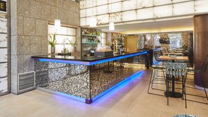 Een moderne bar met een marmeren wand, een bekleed aanrecht en een zithoek met tafels en stoelen.