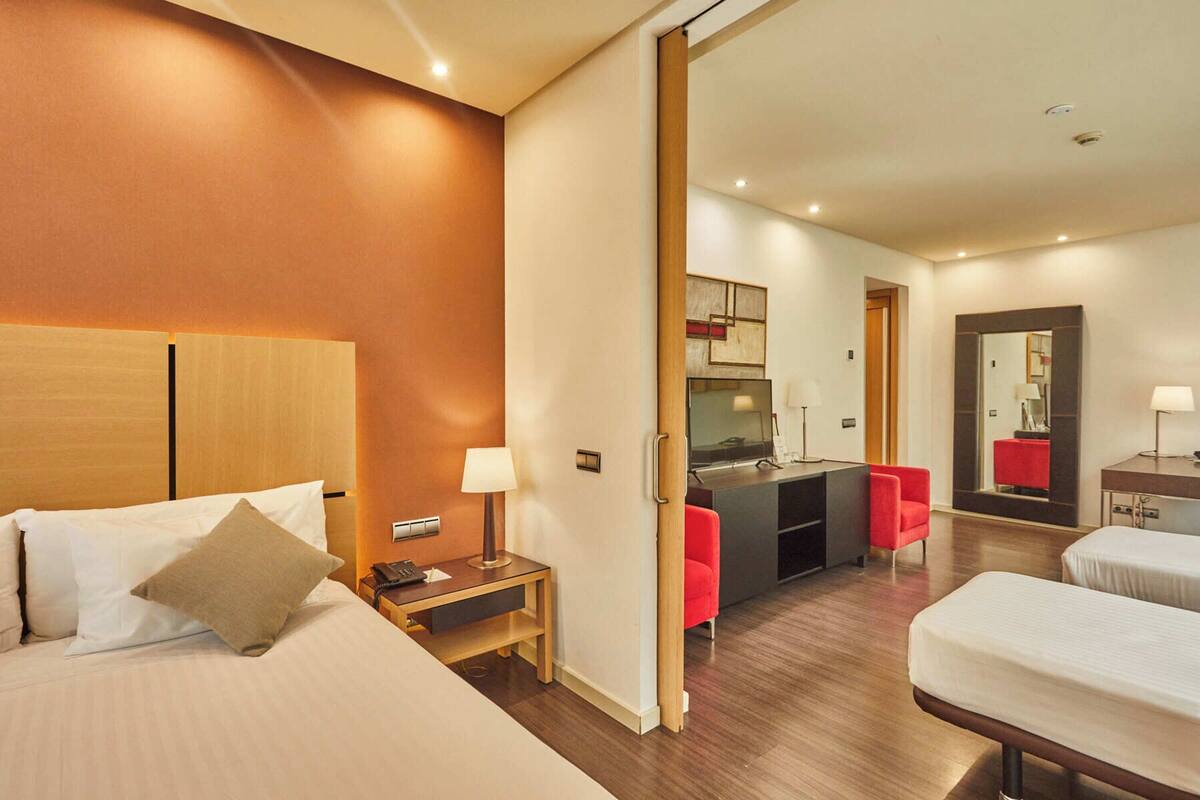 Een hotelkamer met een bed, nachtkastje, lamp en een rode stoel.