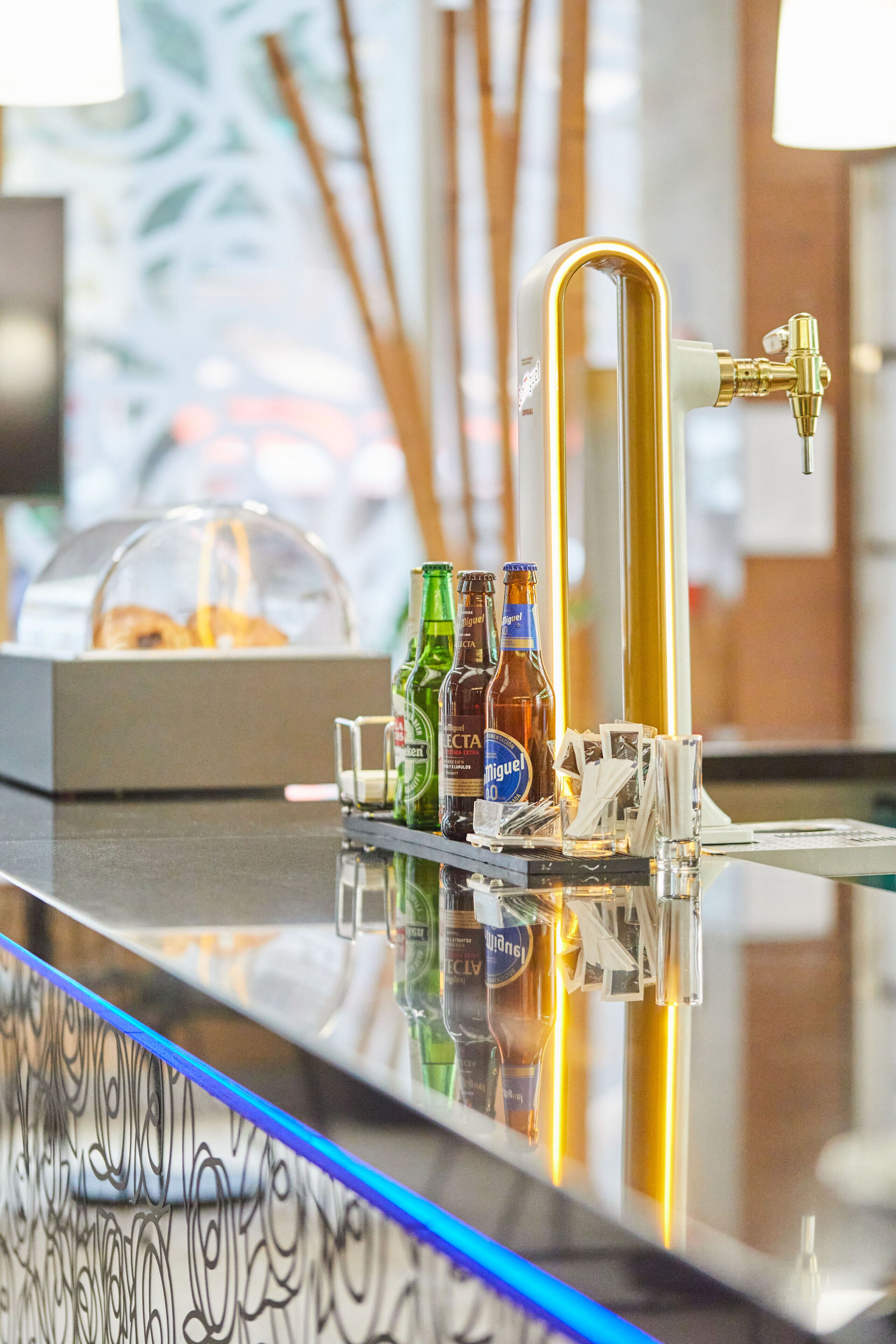 A bar area with a glass counter, bottles of beer, and a tap.