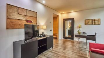 A modern living room with a flat-screen TV, a dark console table, a red chair, and a wooden floor.