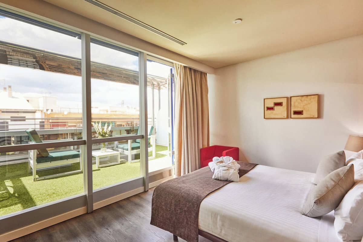 Een hotelkamer met een grote schuifglazen deur die uitkomt op een buitenruimte met uitzicht op gebouwen en een gazon.