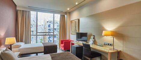 Habitación de hotel con dos camas, un escritorio, una silla, un televisor y una ventana con cortinas.