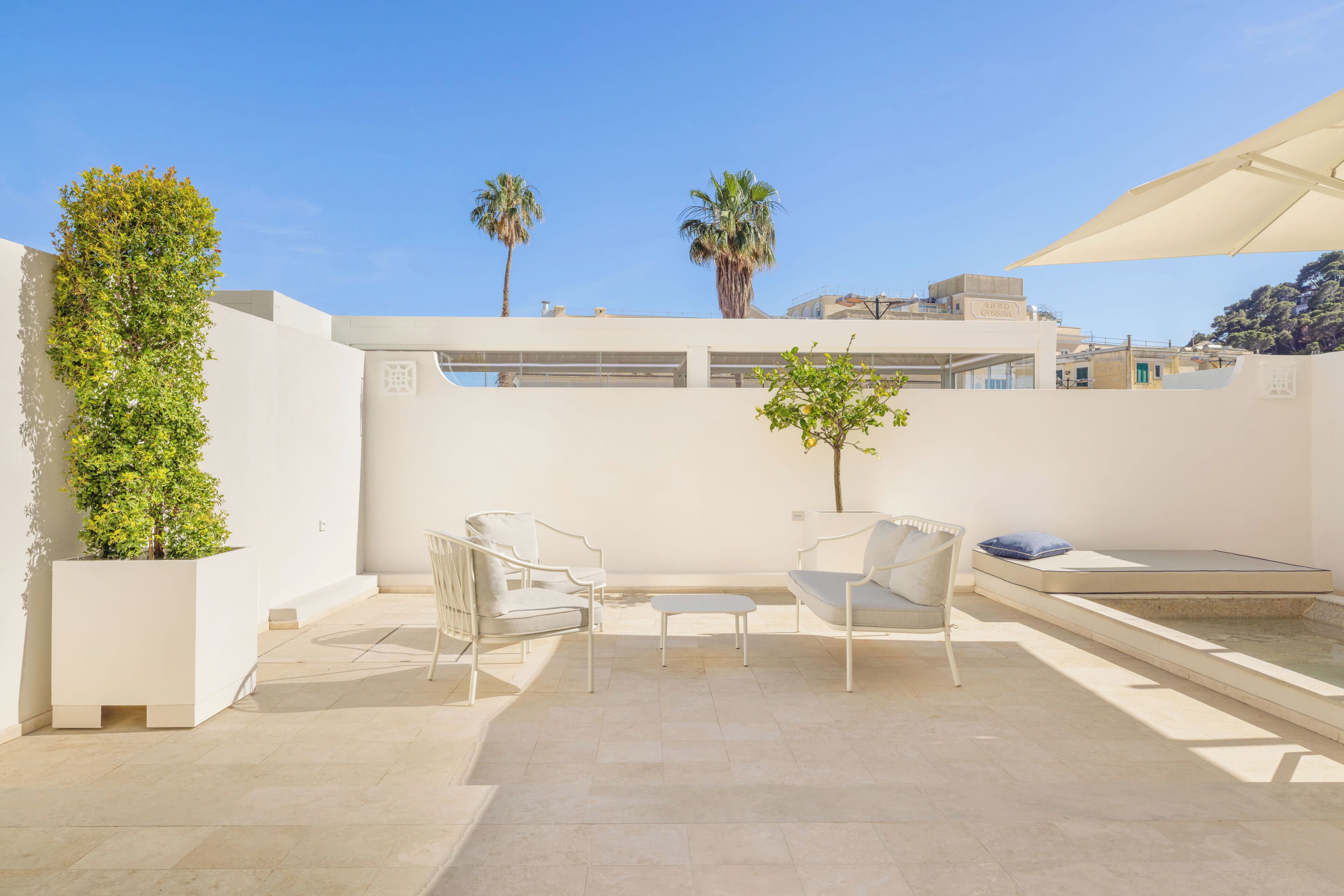 A rooftop terrace with two white chairs, a small table, and a potted plant.