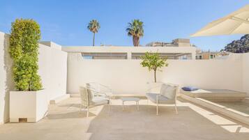 A rooftop terrace with two white chairs, a small table, and a potted plant.