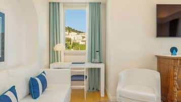 Un soggiorno moderno con un divano bianco, una poltrona bianca, un tavolino in vetro, un televisore montato a parete e vista sugli edifici attraverso la finestra.