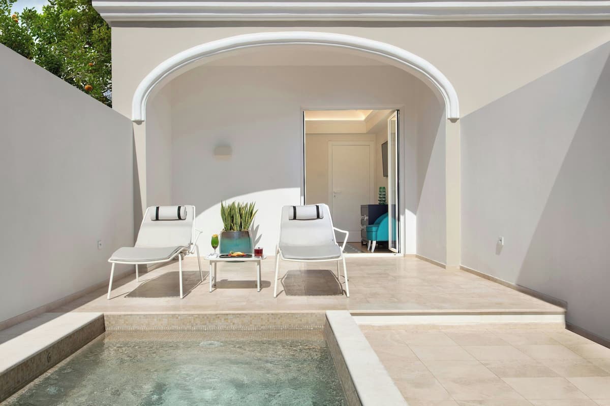 Un espace piscine extérieur moderne, comprenant deux chaises longues et une petite table agrémentée d’une plante.