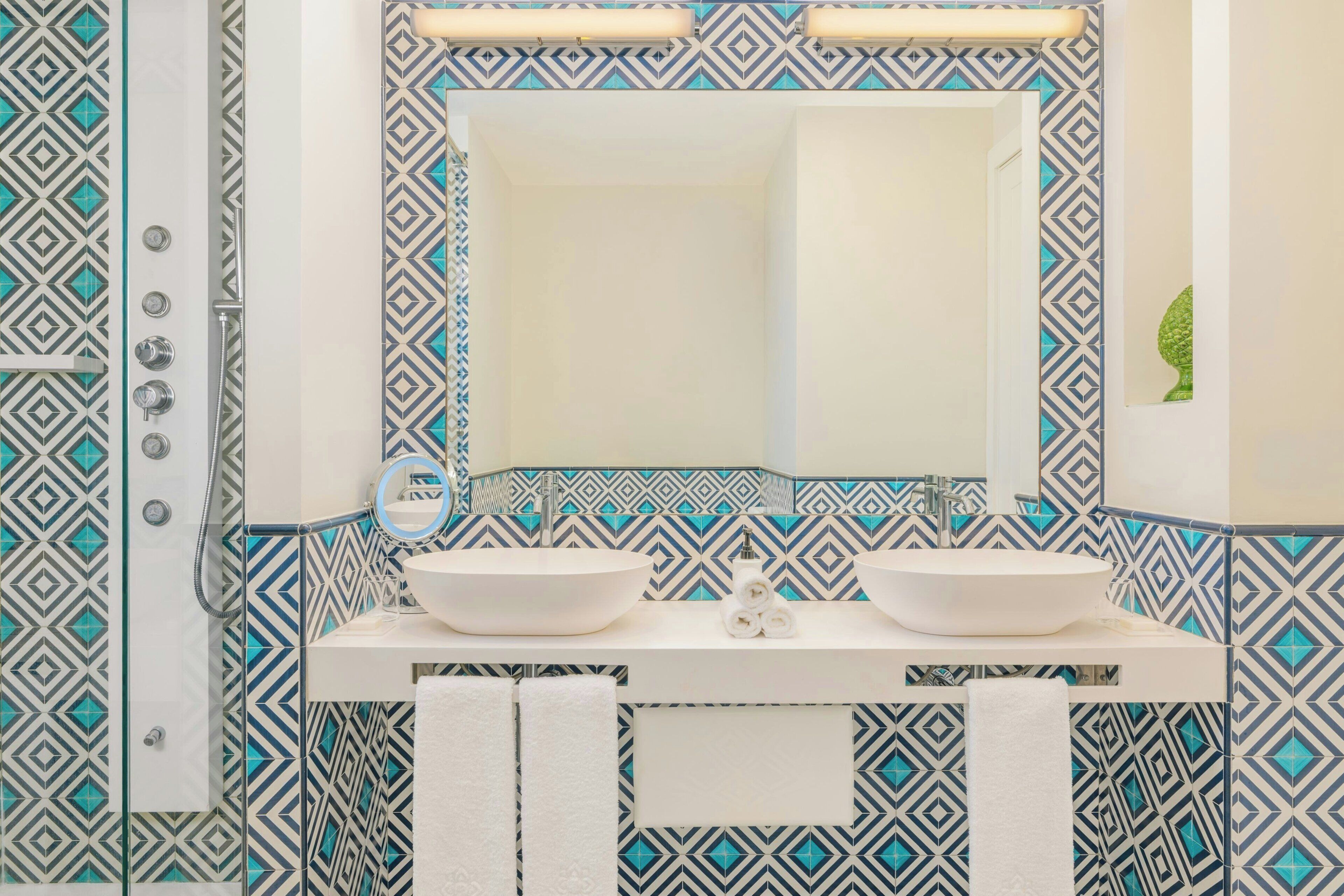 A bathroom with a white sink, two mirrors, and a patterned tile backsplash.