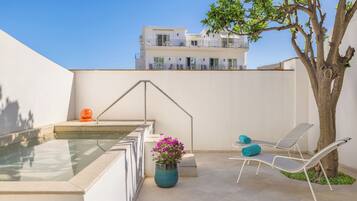 Zona de piscina en la azotea con vista despejada a un edificio, un árbol y una planta en maceta al fondo.