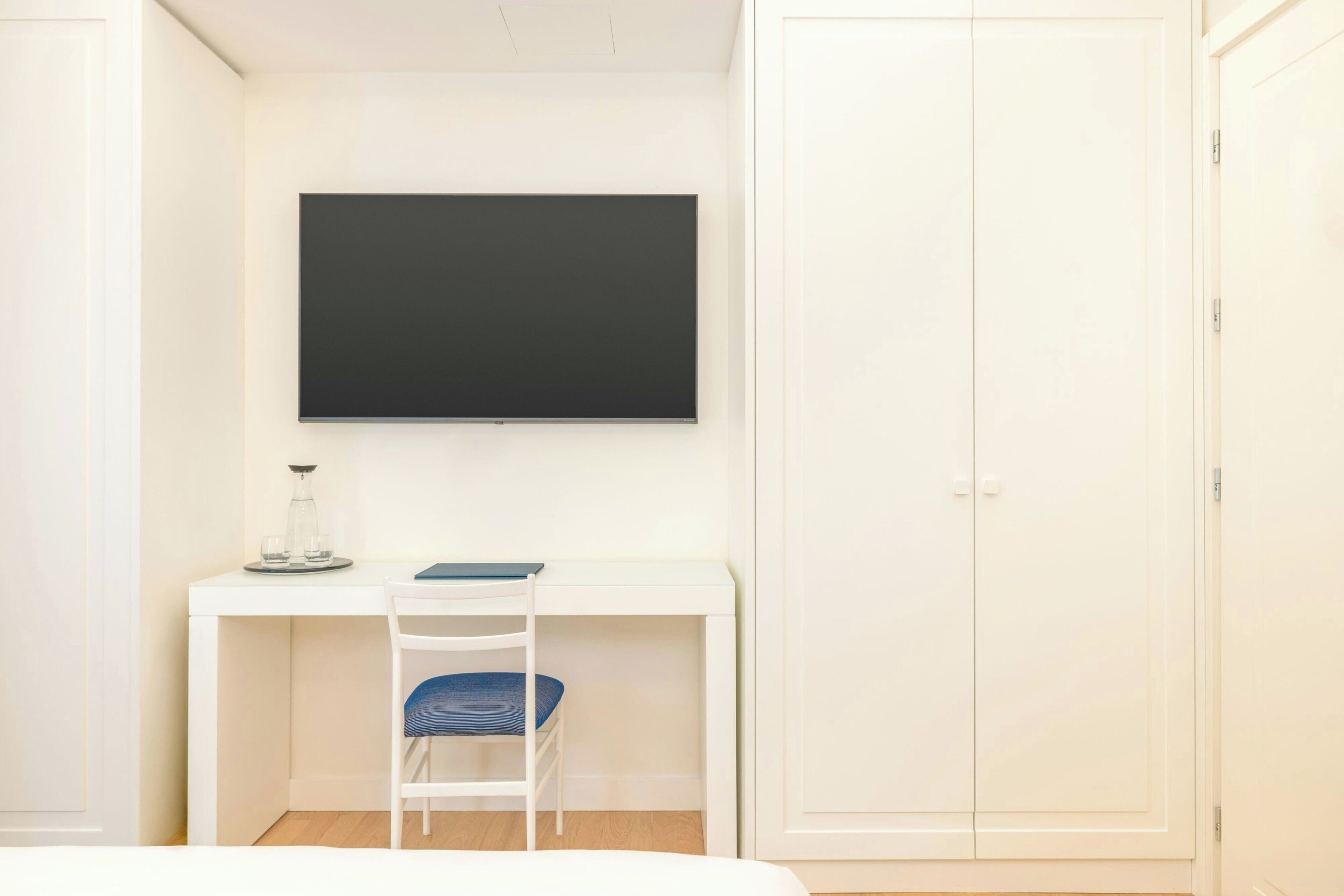 A room with a white desk, a chair, a bed, and a wardrobe.